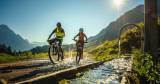 Zwei Radfahrer nutzen die abenteuerlichen Radwege rund um das Alpina Family, Spa & Sporthotel bei strahlendem Sonnenschein. 