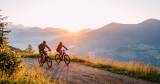 Zwei Radfahrer nutzen die abenteuerlichen Radwege rund um das Alpina Alpendorf bei Sonnenuntergang.