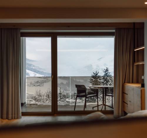 Die Zimmer und Suiten im Alpina Alpendorf bieten Panoramablick über die verschneiten Berge