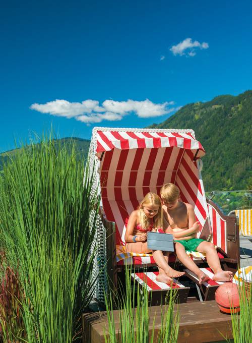 Zwei Kinder sitzen in einem Strandkorb und genießen den Familienurlaub im Salzburger Land. 