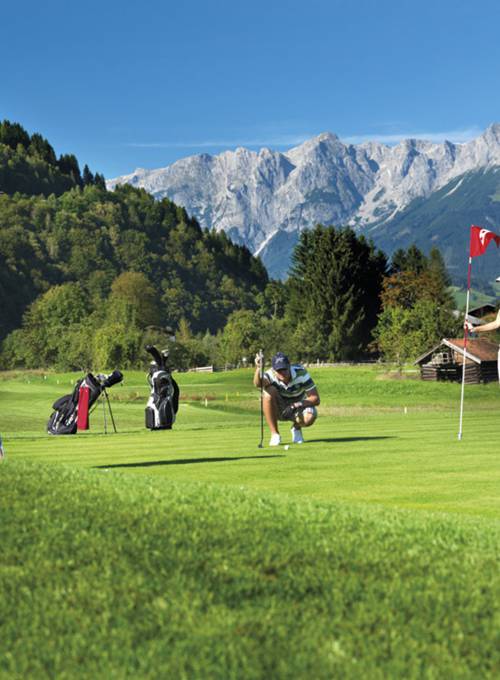 Vor einer wunderschönen Bergkulisse spielt ein Mann Golf in unserem Golfhotel in Österreich. 