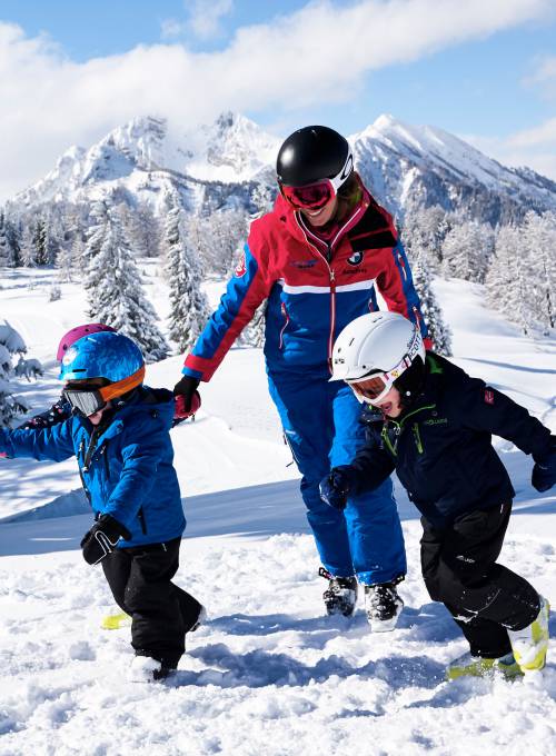 Eine Mutter spielt im Skiurlaub mit ihren Kindern in Österreich im Schnee.