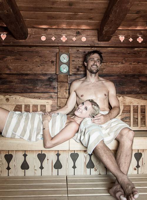 Ein Mann und eine Frau entspannen auf der Holzbank in der Sauna im Alpina Spa Hotel in Salzburg. 