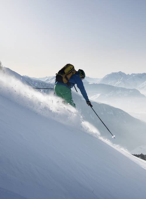 Ein Mann fährt mit Geschwindigkeit auf Skiern die Piste direkt neben dem Hotel Alpina herunter. 