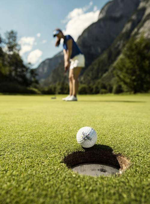 Vor einer wunderschönen Bergkulisse spielt ein Mann Golf in unserem Golfhotel in Österreich. 