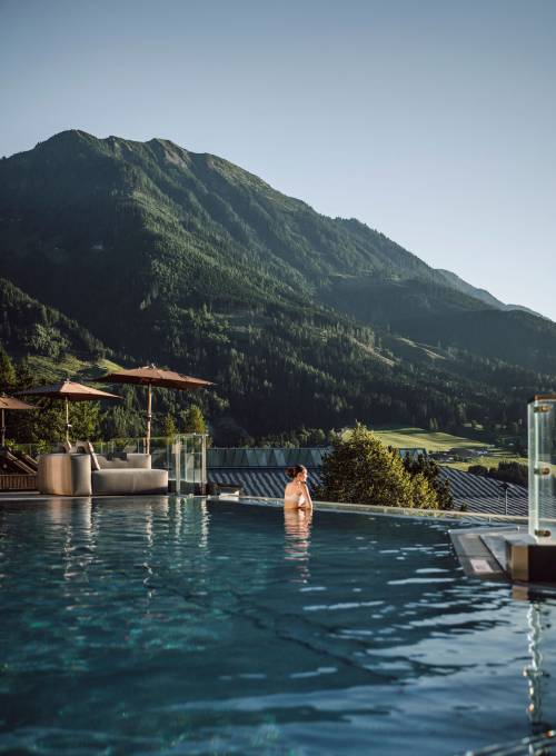 Eine Frau genießt die Berglandschaft beim Schwimmen im Infinity outdoor Pool.